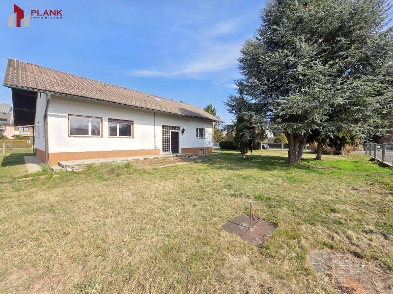 Rückansicht des Hauses mit weitläufigem Garten und Zugang zum Gebäude, umgeben von Bäumen.