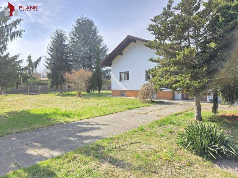 Seitenansicht des Hauses mit gepflasterter Auffahrt und weitläufigem Rasenbereich unter blauem Himmel.