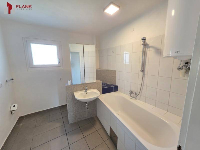 Geräumiges Badezimmer mit Badewanne, Waschbecken, Spiegelschrank und einem Fenster für Tageslicht.