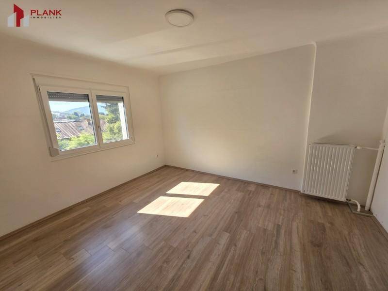 Helles Zimmer mit Laminatboden, Heizkörper und einem Fenster mit Blick auf die Umgebung.