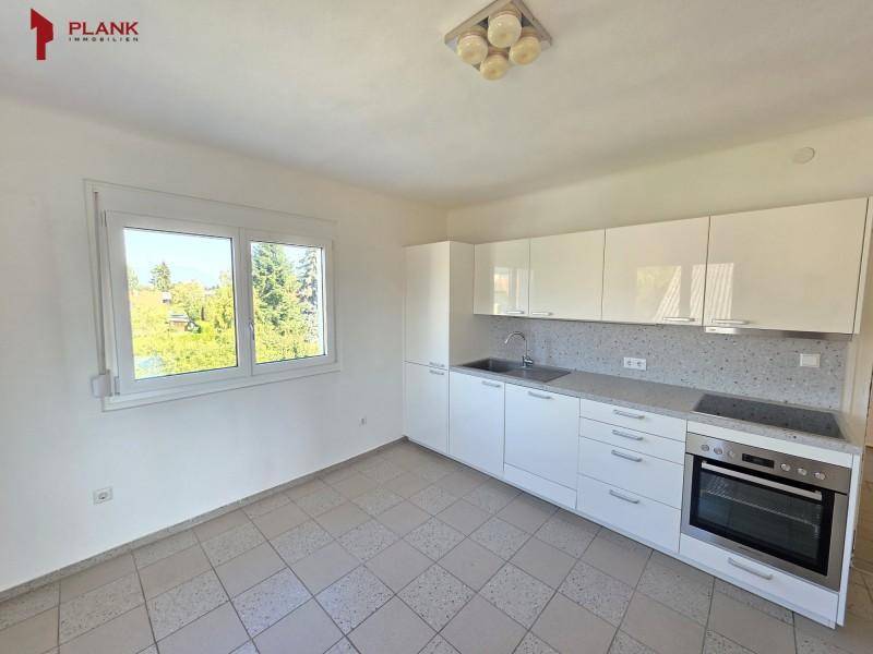 Moderne Küche mit weißen Hochglanzschränken, integriertem Backofen und einem Fenster mit Ausblick.