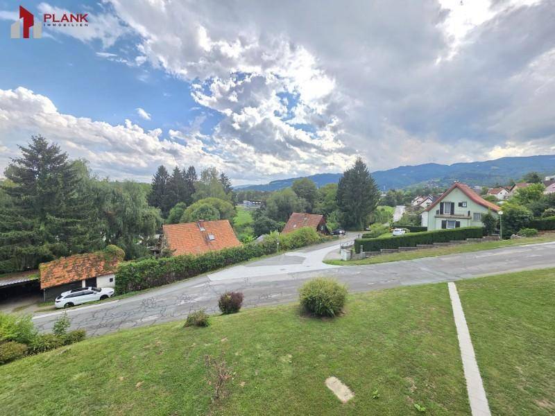 Weitläufiger Blick über eine grüne Wohnsiedlung mit Häusern und Bergen im Hintergrund.