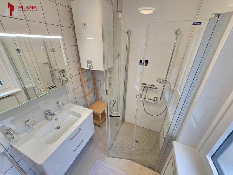 Modernes Badezimmer mit Duschkabine, weißem Waschtisch und großem Spiegel.