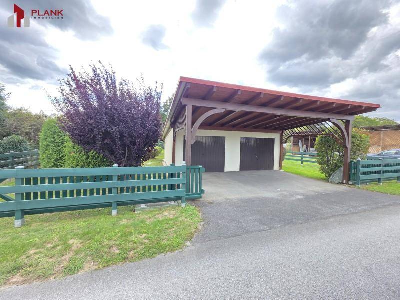 Doppelgarage mit Carport und gepflasterter Zufahrt, umgeben von Grünflächen.