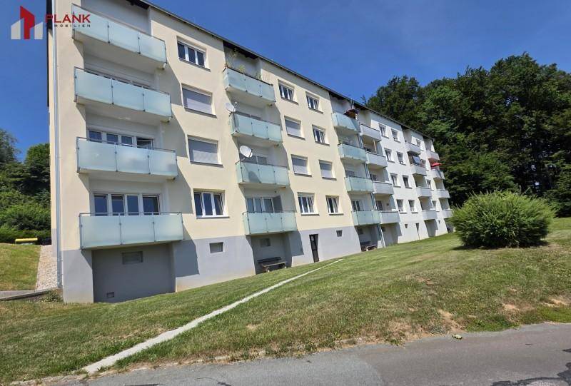Mehrstöckiges Wohngebäude mit Balkonen und einer hellen Fassade, eingebettet in eine grüne Umgebung.