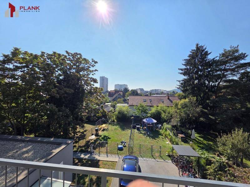 Sonniger Ausblick vom Balkon auf eine grüne Umgebung mit Bäumen und entfernten Stadtgebäuden.