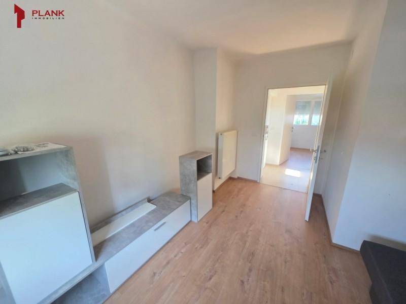 Heller Innenraum mit modernem Möbelstück und Laminatboden, der zu einem weiteren Zimmer führt.