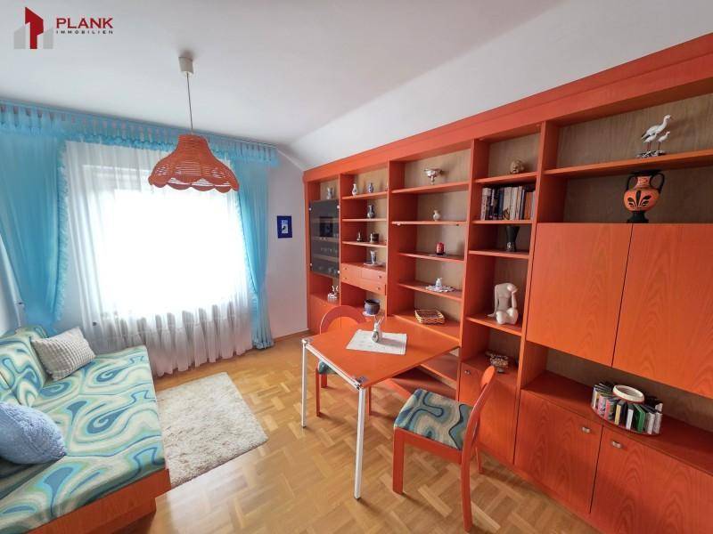 Helles Wohnzimmer mit farbenfroher Dekoration, Holzparkett und großem Bücherregal.