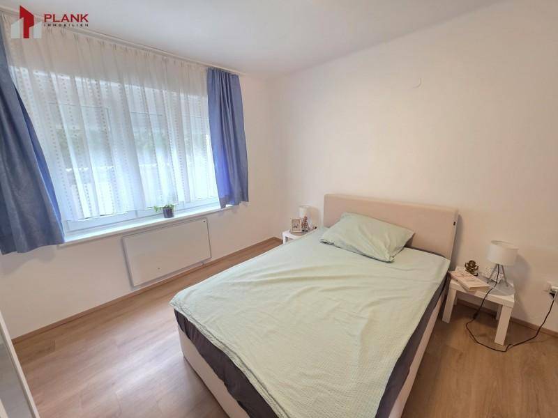 Helles Schlafzimmer mit Einzelbett, Nachttischen und Fenster mit blauen Vorhängen.