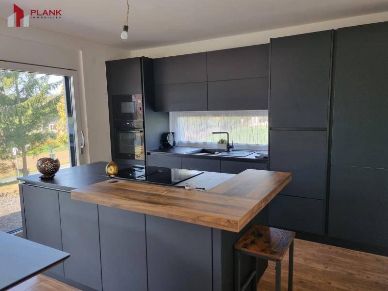 Moderne schwarze Küche mit Kochinsel, Holzarbeitsplatte und integrierten Geräten.