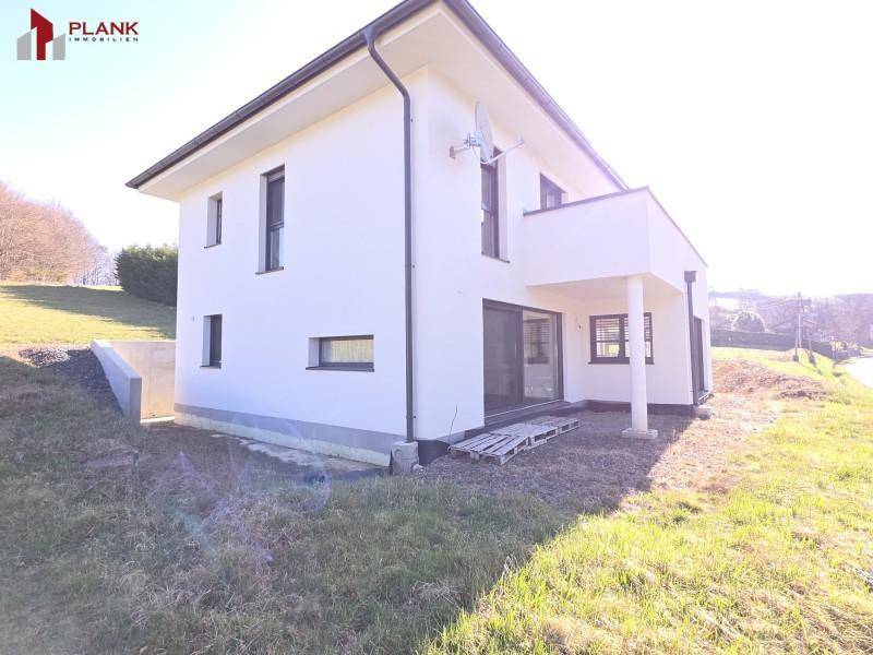 Modernes Einfamilienhaus mit weißer Fassade, Balkon und Zugang zum Garten.