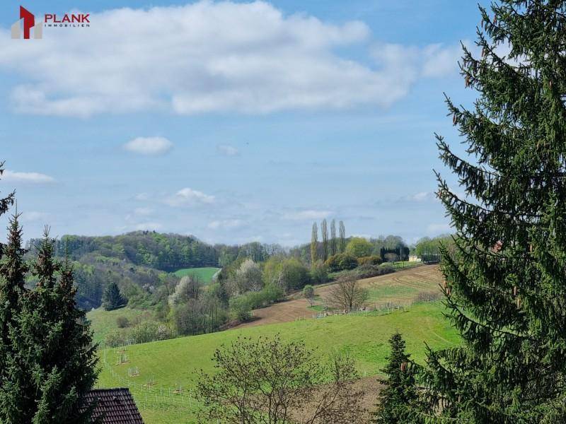 Weitläufiger Blick über grüne Hügel und Felder unter blauem Himmel.