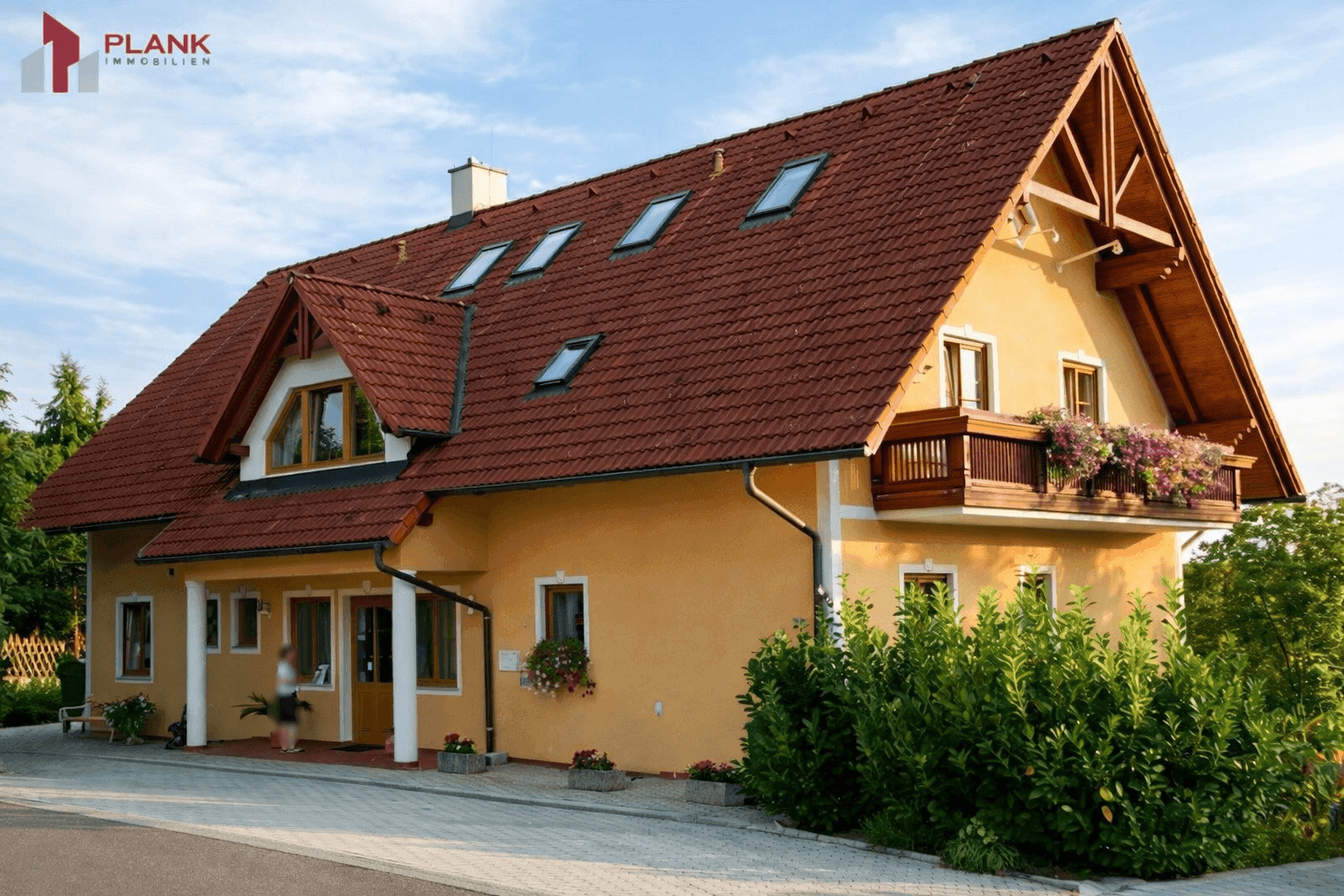 Traditionelles Haus mit gelber Fassade, rotem Ziegeldach und Balkon mit Blumenkästen.