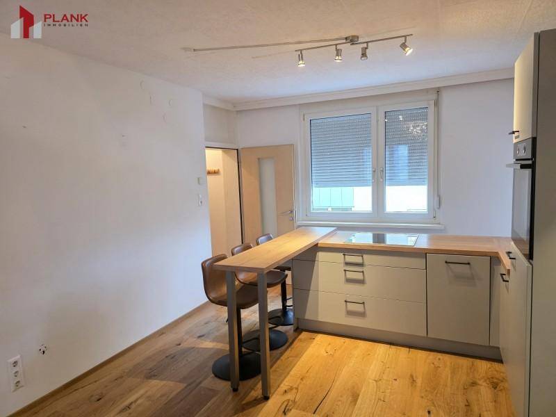 Funktionale Einbauküche mit Holzarbeitsplatte, Frühstücksbar und Fenster mit Rollläden.