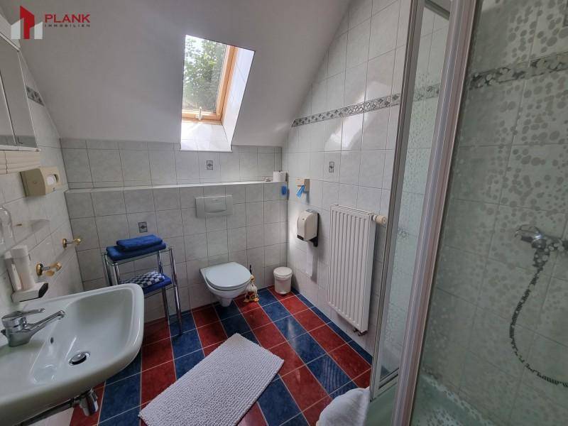 Badezimmer im Dachgeschoss mit Dusche, WC, Waschbecken und farbigen Fliesen.