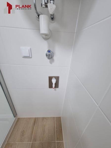 Detaillierte Ansicht des Duschbereichs mit weißen Wandfliesen und modernen Armaturen.