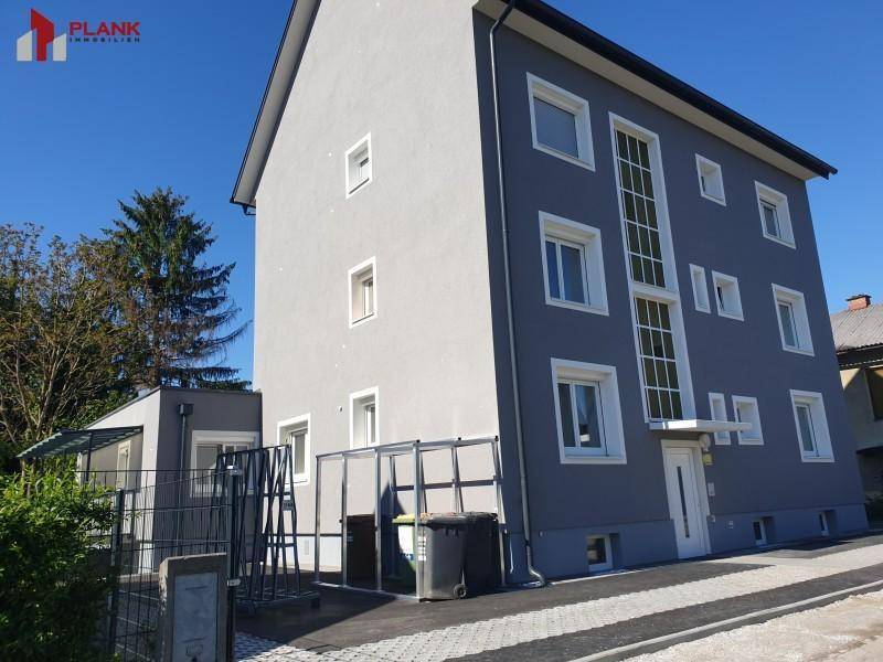 Modernes Mehrfamilienhaus mit grauer Fassade, vielen Fenstern und gepflegtem Eingangsbereich.