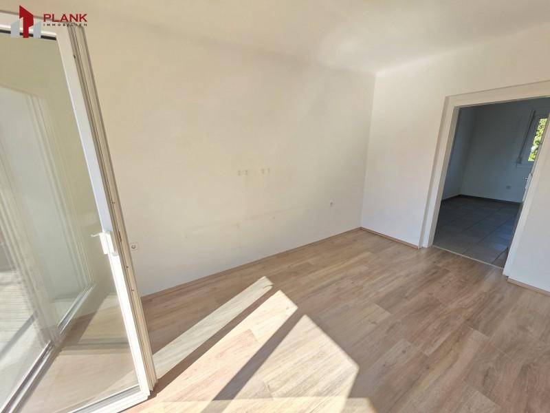 Helles Zimmer mit Laminatboden und weiß gestrichenen Wänden, mit großem Fenster und Tür.