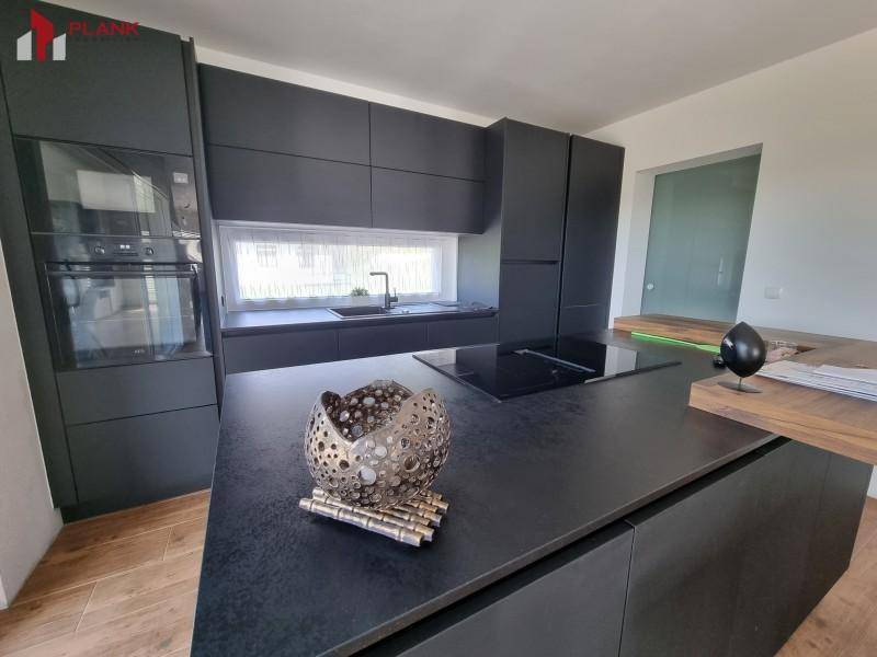 Moderne schwarze Küche mit Kochinsel, dunkler Arbeitsplatte und integrierten Geräten.