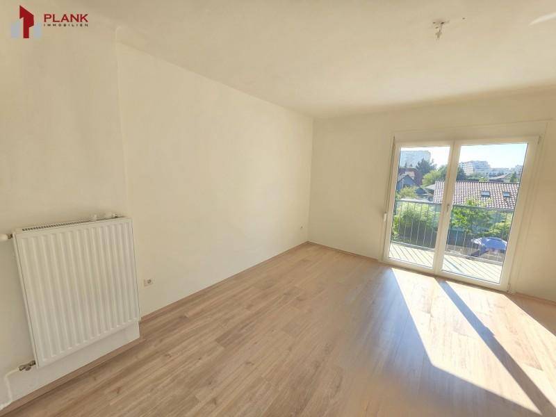 Helles Zimmer mit Laminatboden, weiß gestrichenen Wänden und Zugang zu einem Balkon mit Ausblick.