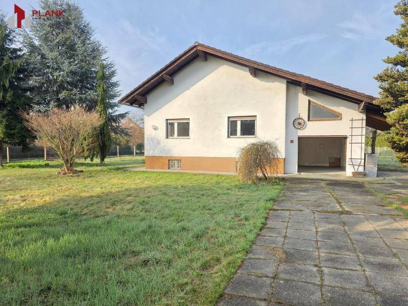 Ansicht des Hauses mit gepflasterter Auffahrt und integrierter Garage, umgeben von Grünflächen.