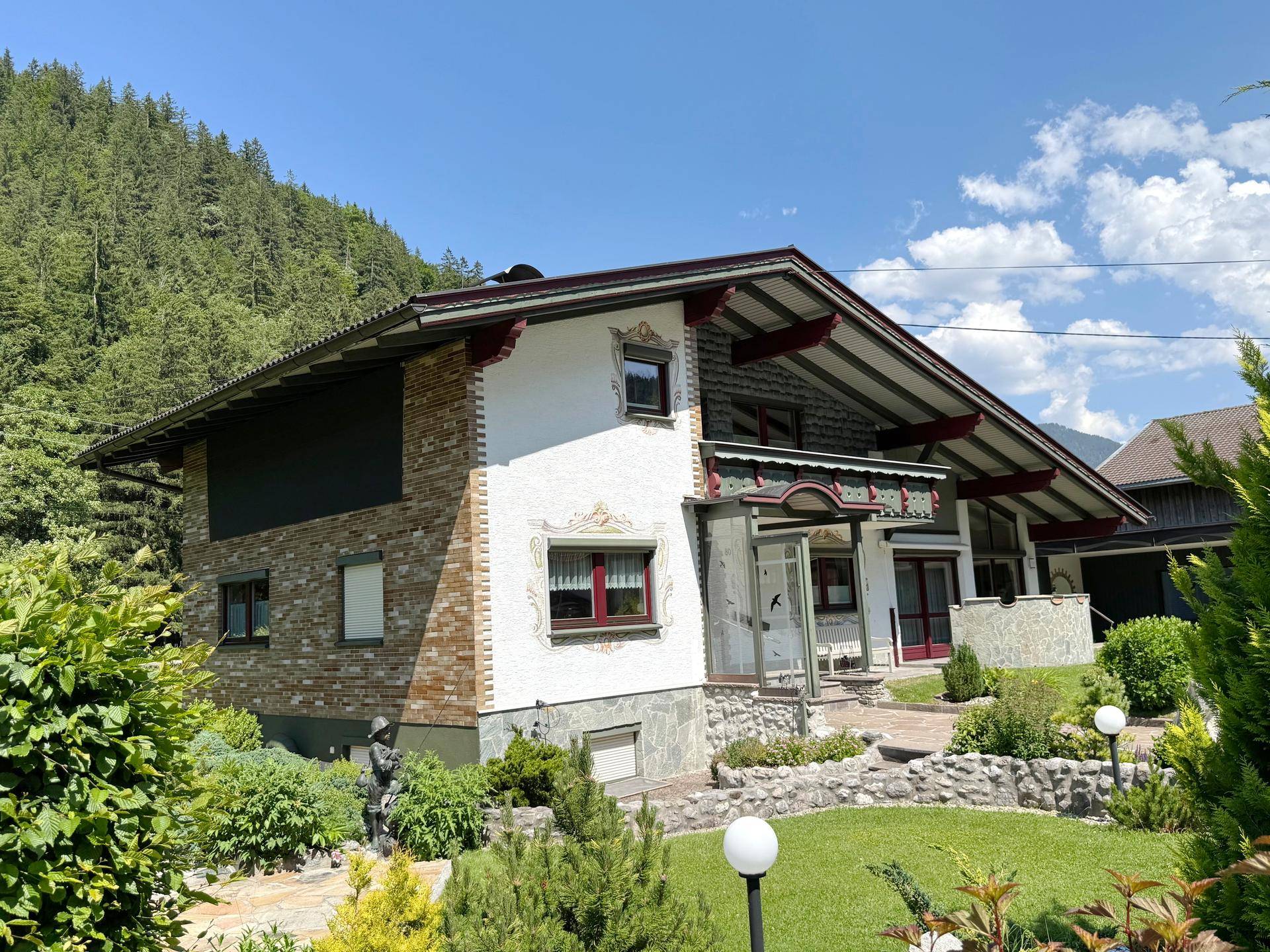 Seitenansicht des Hauses mit Steinverkleidung, gepflegtem Rasen und dekorativen Gartenleuchten.