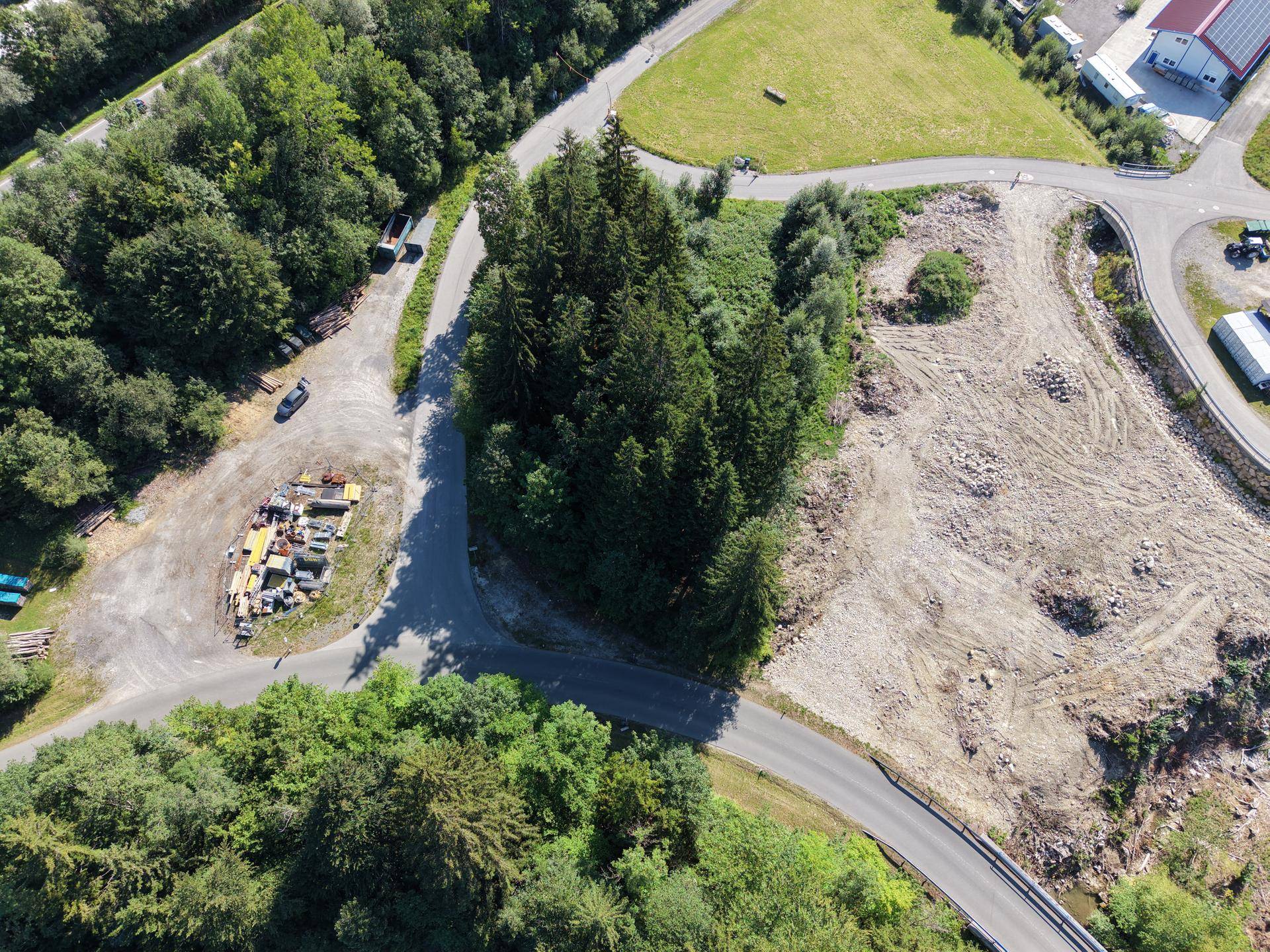 Weitläufige Luftaufnahme eines gerodeten Grundstücks umgeben von Wald, Straßen und ländlicher Bebauung in sonniger Lage.
