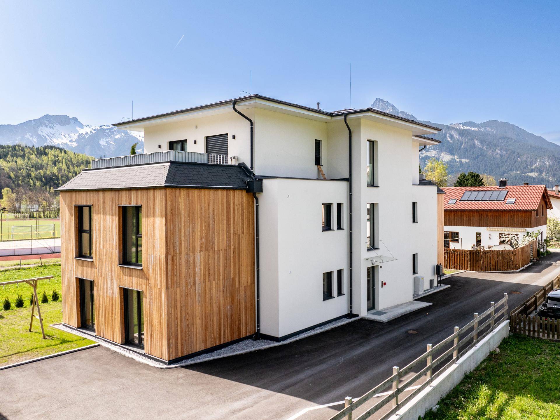 Eingangsbereich des modernen Wohnhauses mit Zufahrt und Panoramablick auf die umliegende Bergwelt.