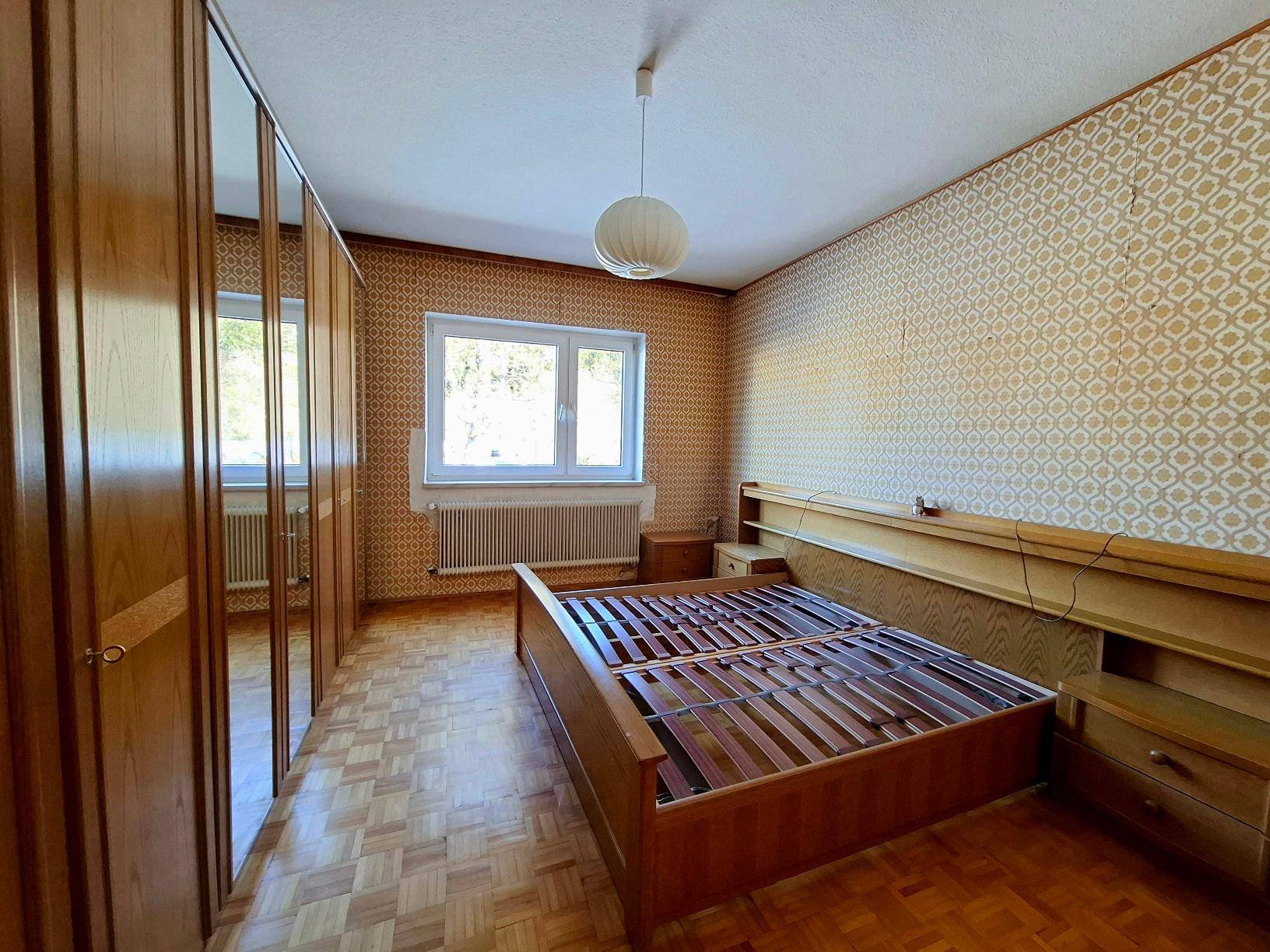 Schlafzimmer mit gemusterten Tapeten, Parkettboden und integrierten Holzschränken.