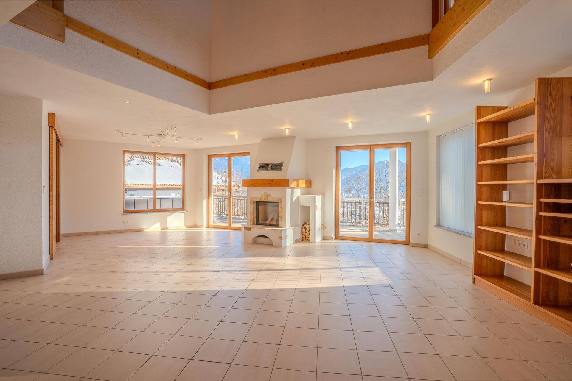 Geräumiges Wohnzimmer mit Fliesenboden, Kamin und großen Fenstern mit Zugang zum Balkon und Bergblick.