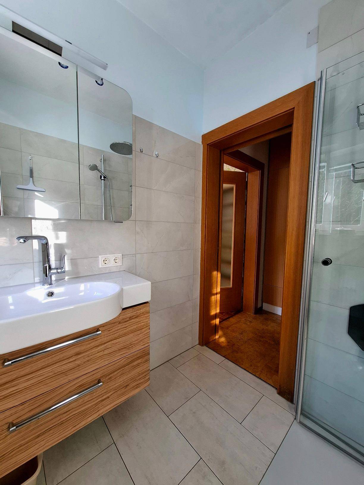 Modernes Badezimmer mit Waschtisch, Spiegelschrank und begehbarer Dusche.