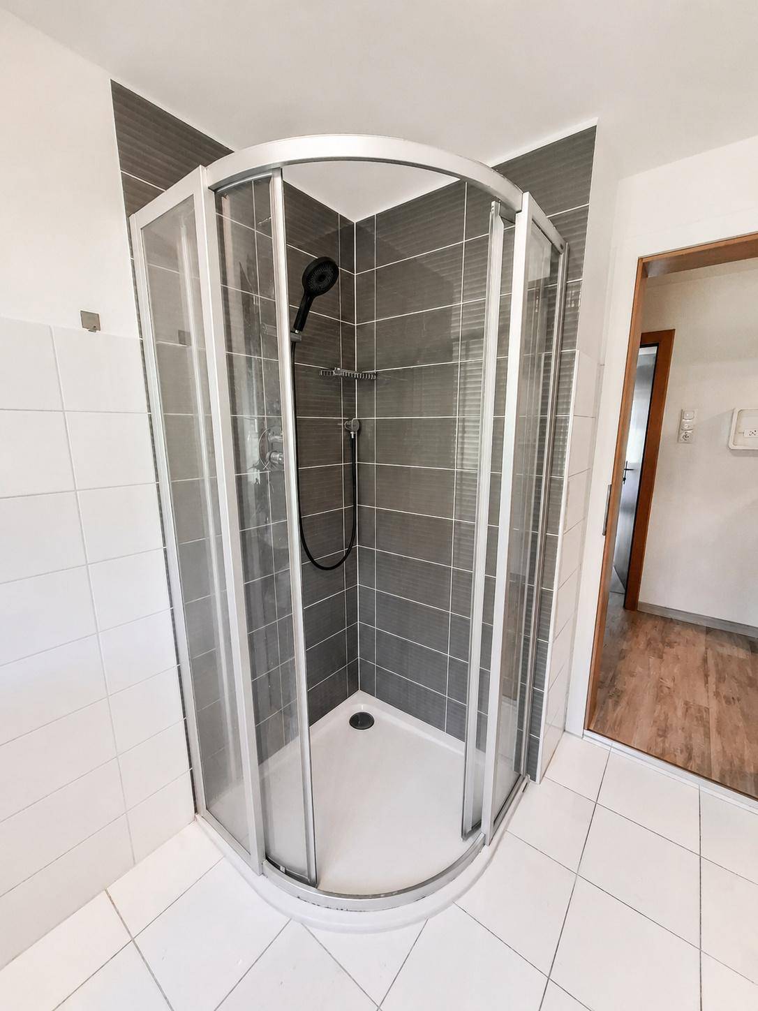 Moderne Duschkabine mit grauen Wandfliesen und weißem Boden in einem hellen Badezimmer.