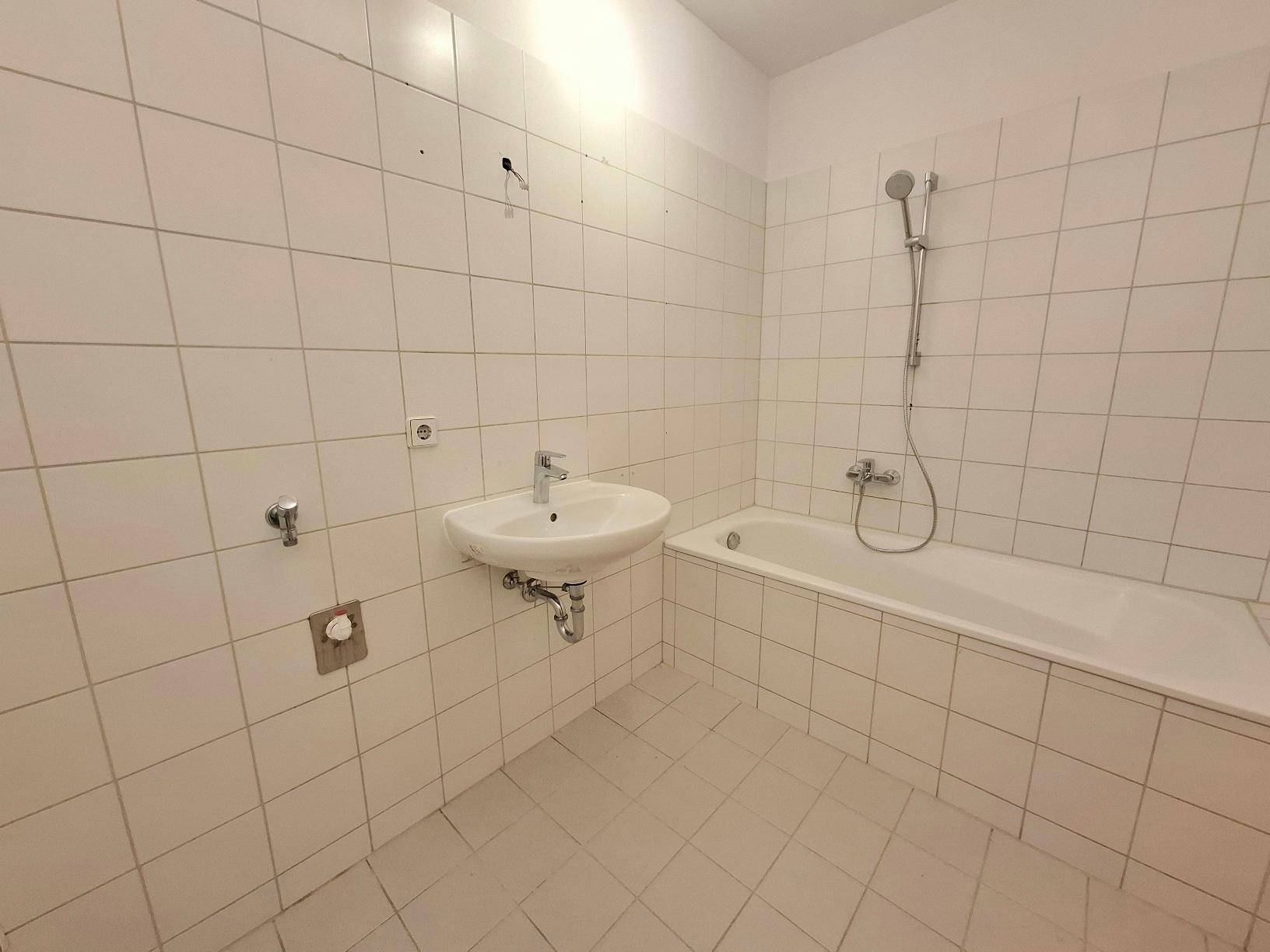 Badezimmer mit weißen Fliesen, einer Badewanne inklusive Duschfunktion und einem Waschbecken.