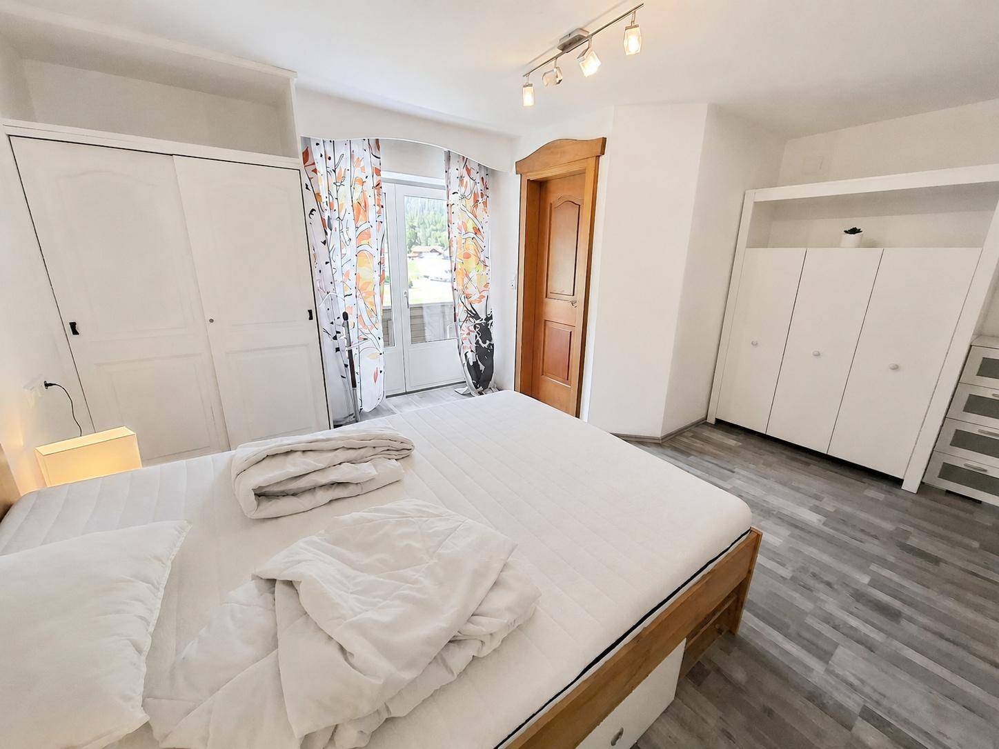 Geräumiges Schlafzimmer mit viel Stauraum in weißen Kleiderschränken und hellem Holzfußboden.