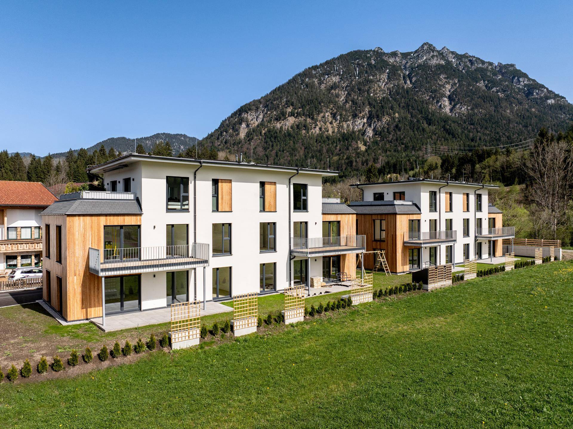 Mehrere moderne Neubauten mit Holzfassaden und Balkonen in alpiner Umgebung.