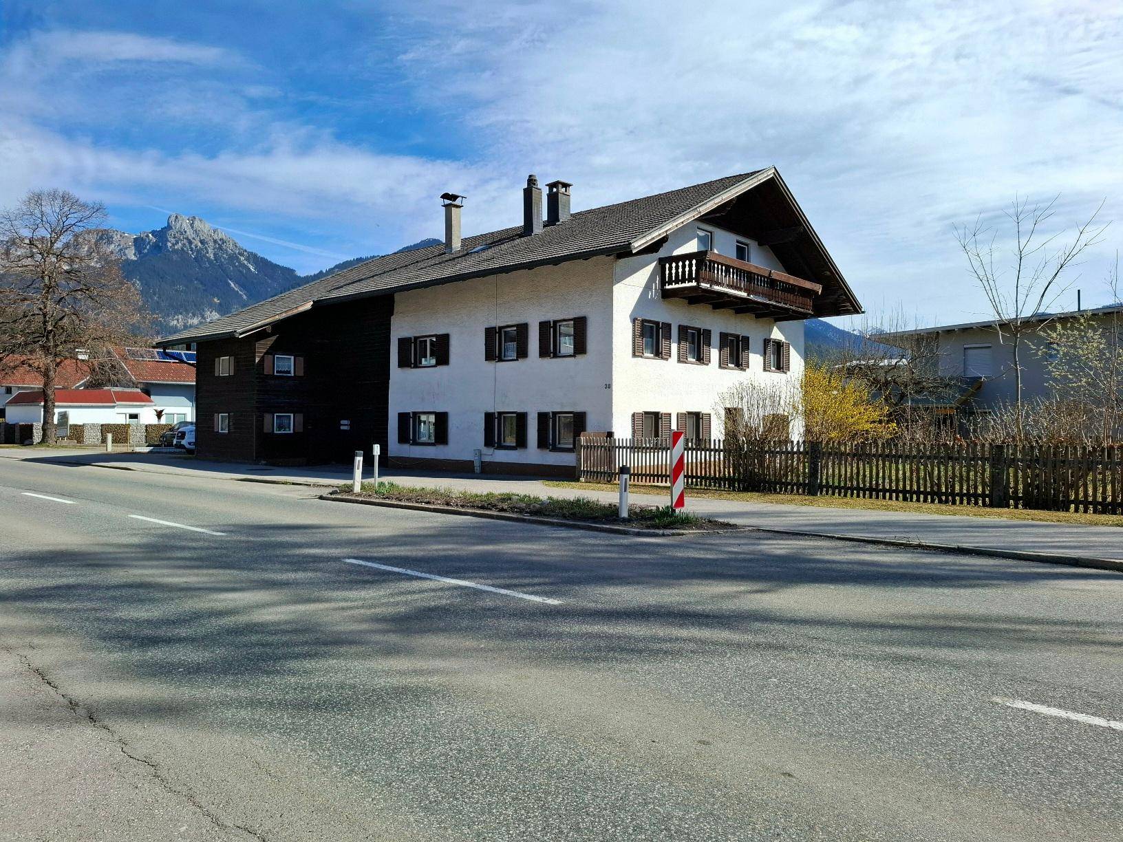 Traditionelles Wohnhaus mit Satteldach und Holzbalkon, gelegen an einer ruhigen Straße mit Bergblick.