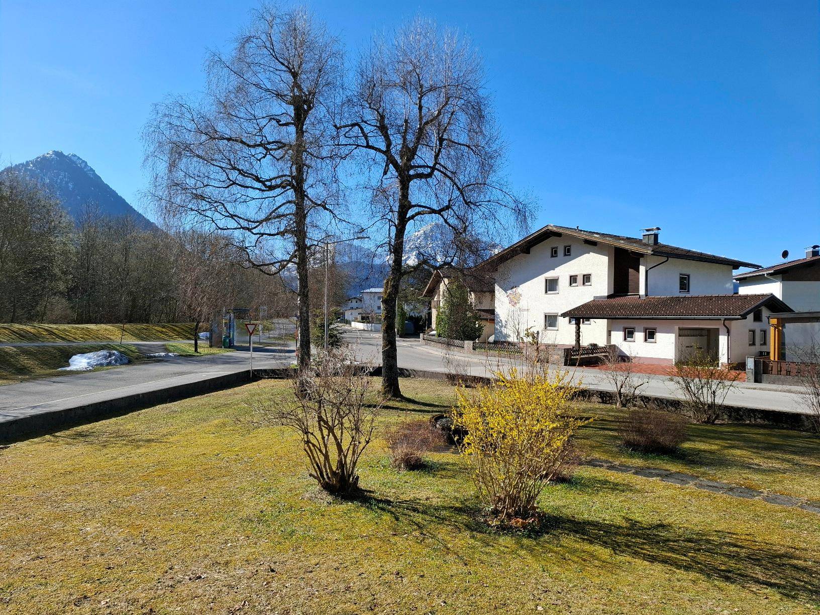 Weitläufiger Blick auf die umliegende Berglandschaft und benachbarte Häuser unter strahlend blauem Himmel.