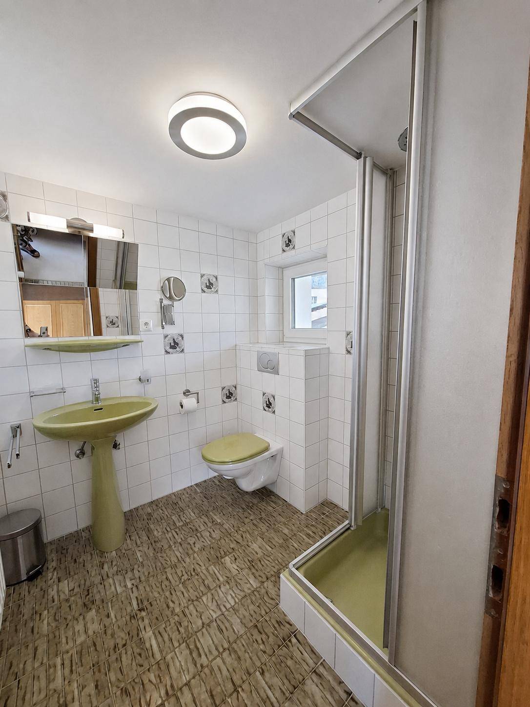 Badezimmer mit grünen Sanitärobjekten, weißen Fliesen und Duschkabine.