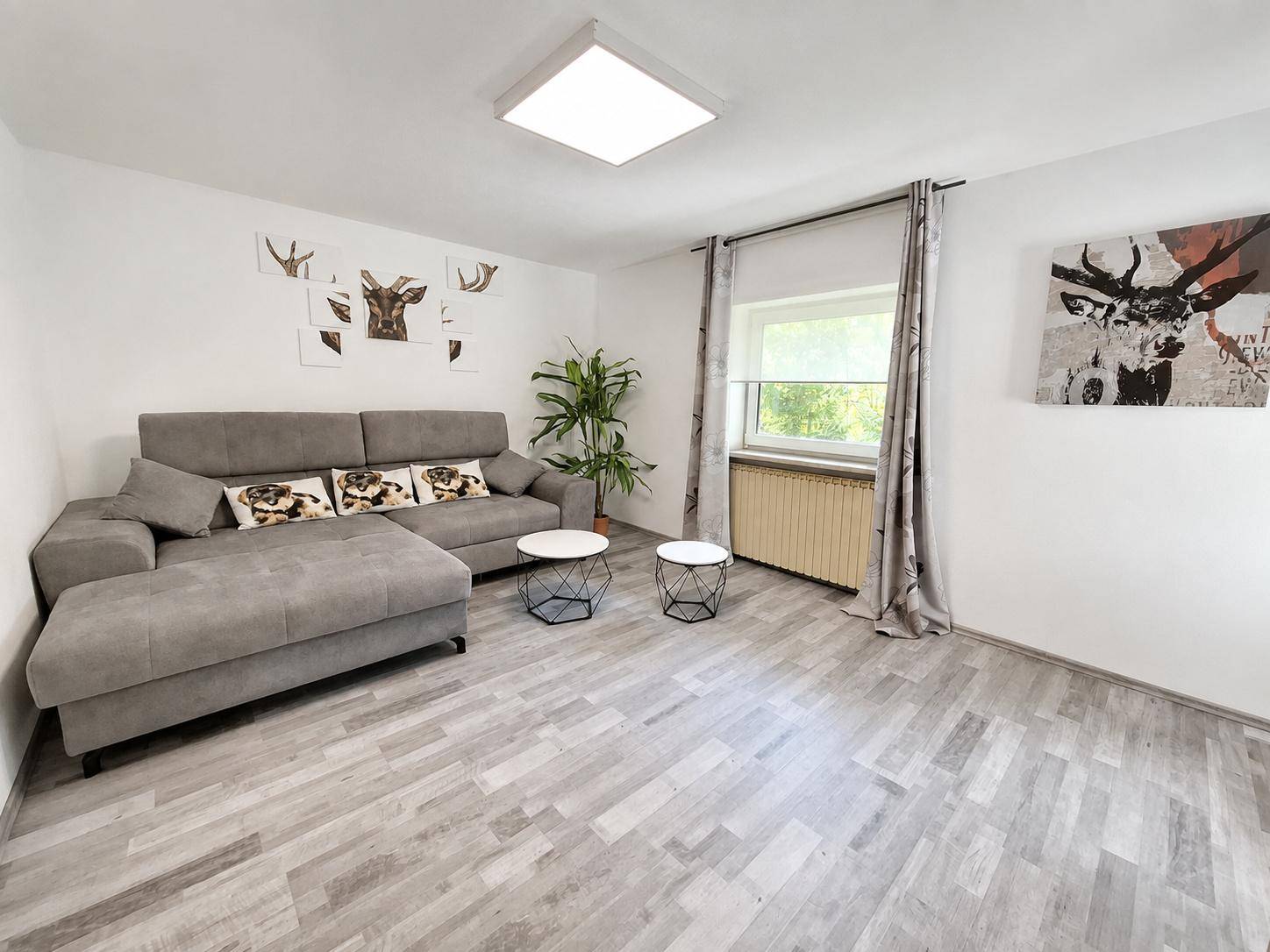 Gemütliches Wohnzimmer mit grauem Ecksofa, hellem Holzfußboden und Hirsch-Wanddekoration.