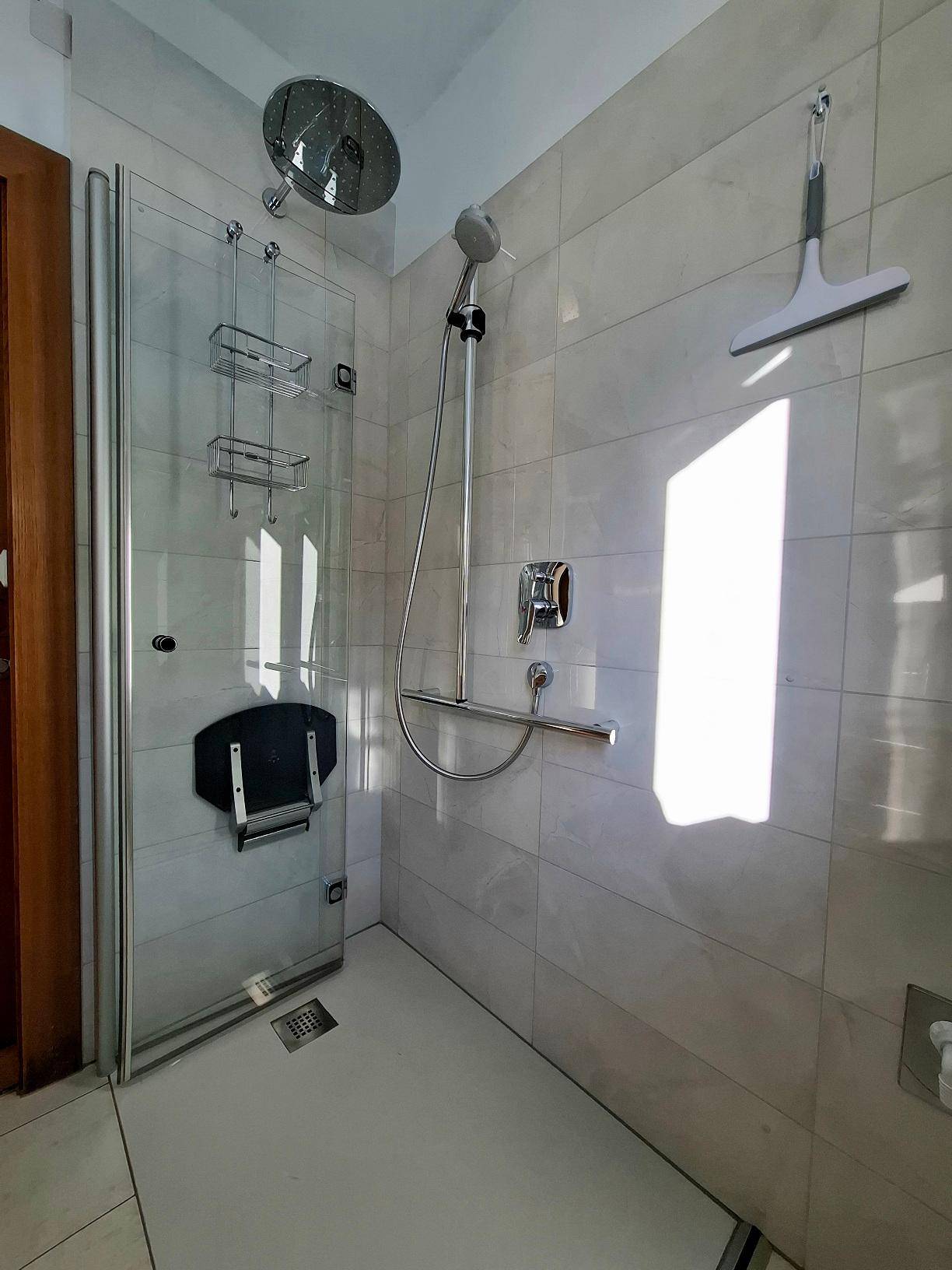 Barrierefreie Dusche mit Regenduschkopf, Haltegriffen und Duschsitz für Komfort und Sicherheit.