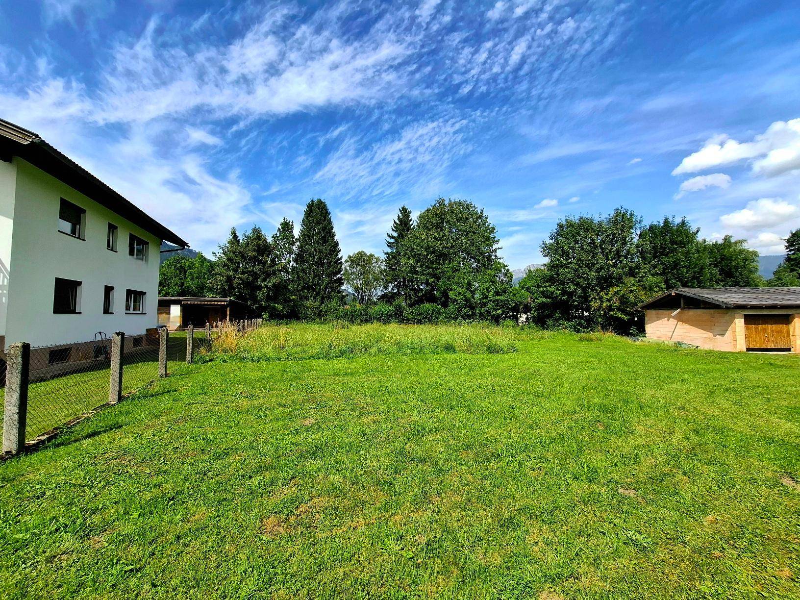 Seitenansicht des Hauses mit weitläufiger grüner Rasenfläche und angrenzendem Zaun.