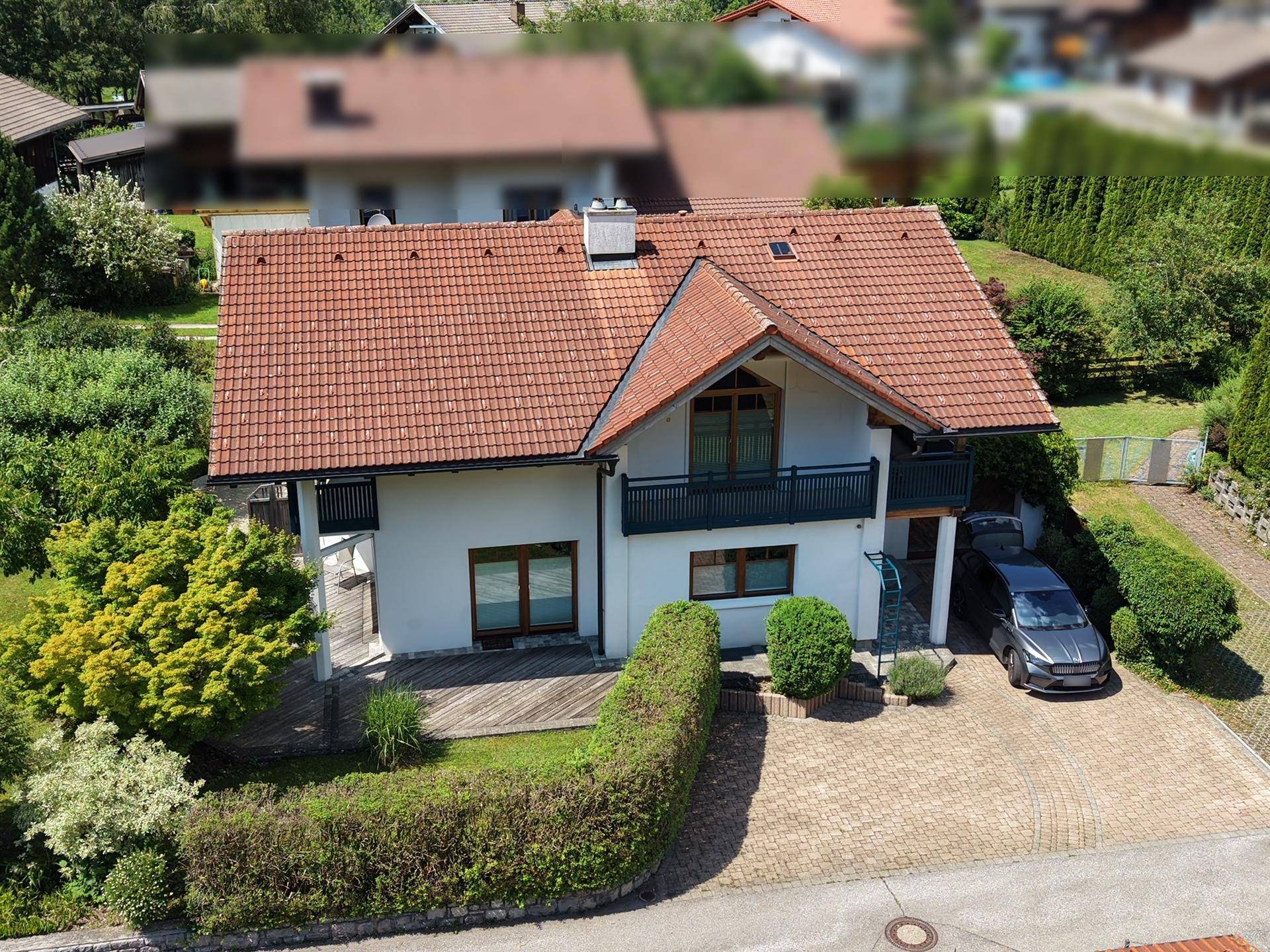 Vorderansicht eines Einfamilienhauses mit gepflasterter Auffahrt, Hecke und Bergblick im Hintergrund.