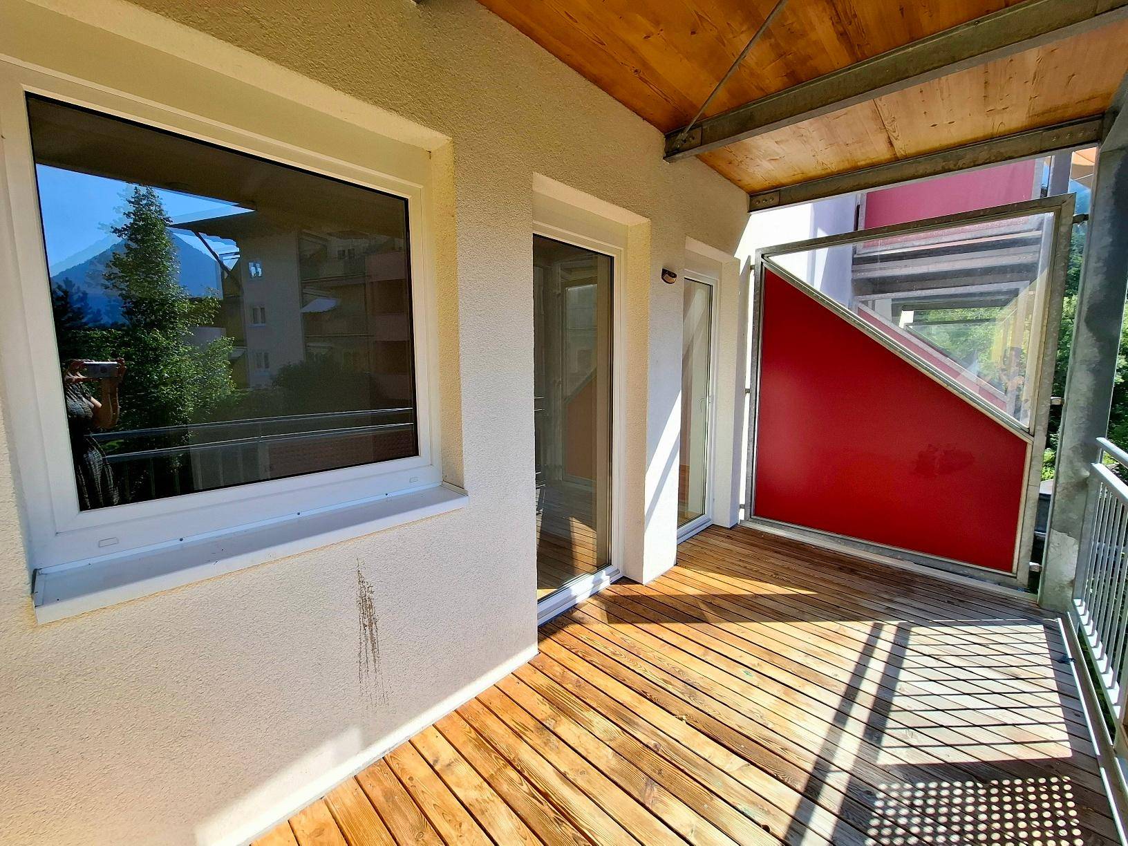 Sonnenverwöhnter Balkon mit Holzboden und einer roten Seitenwand, ideal zum Entspannen im Freien.