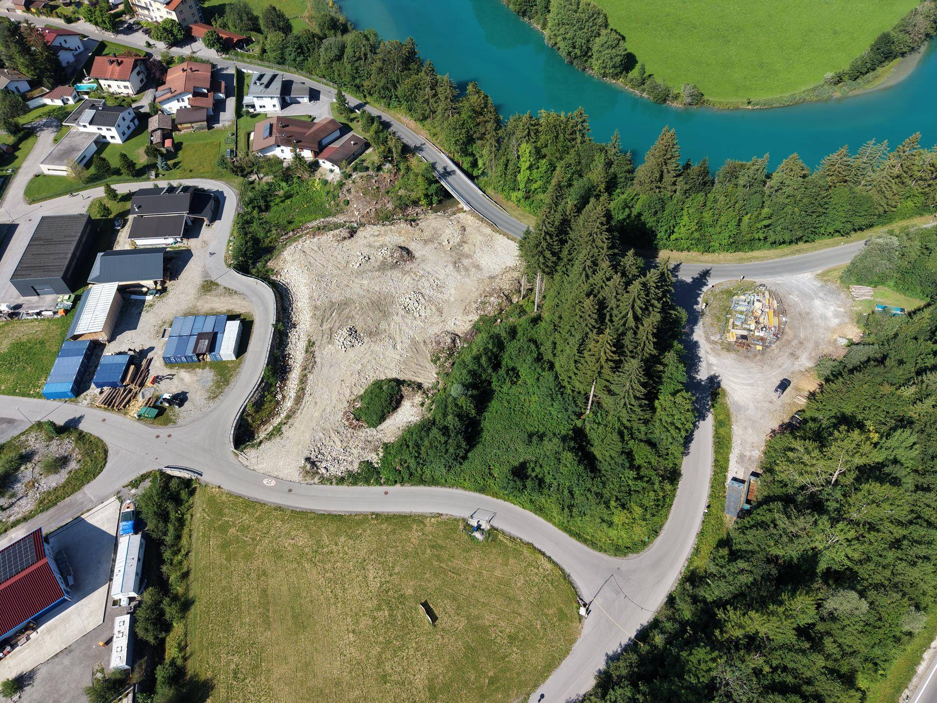 Panoramische Luftaufnahme eines großen Baugrundstücks mit Fluss, Wald und angrenzenden Wohn- und Gewerbegebieten.