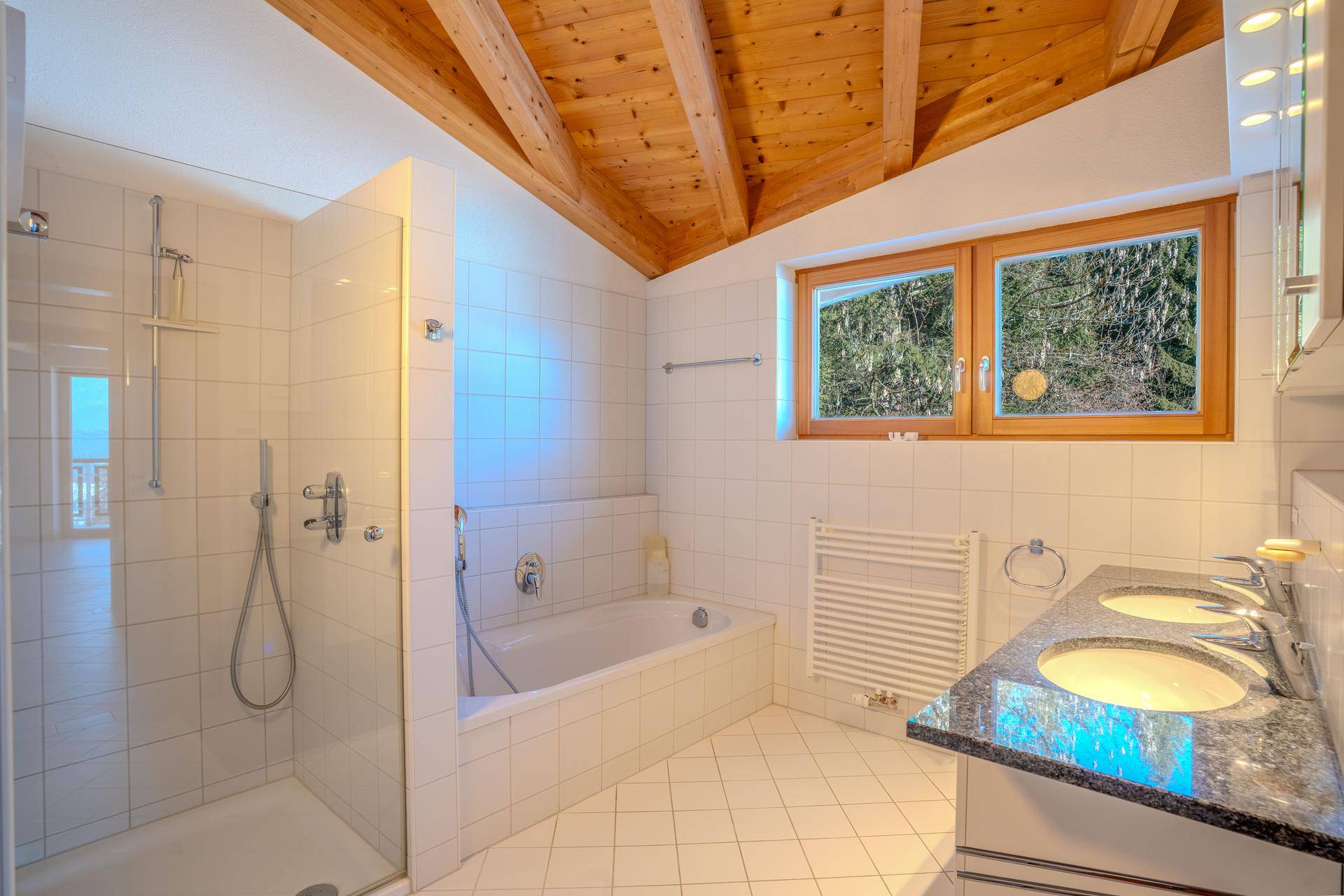 Geräumiges Badezimmer mit weißen Fliesen, Badewanne, begehbarer Dusche und Doppelwaschbecken unter Holzdecke.