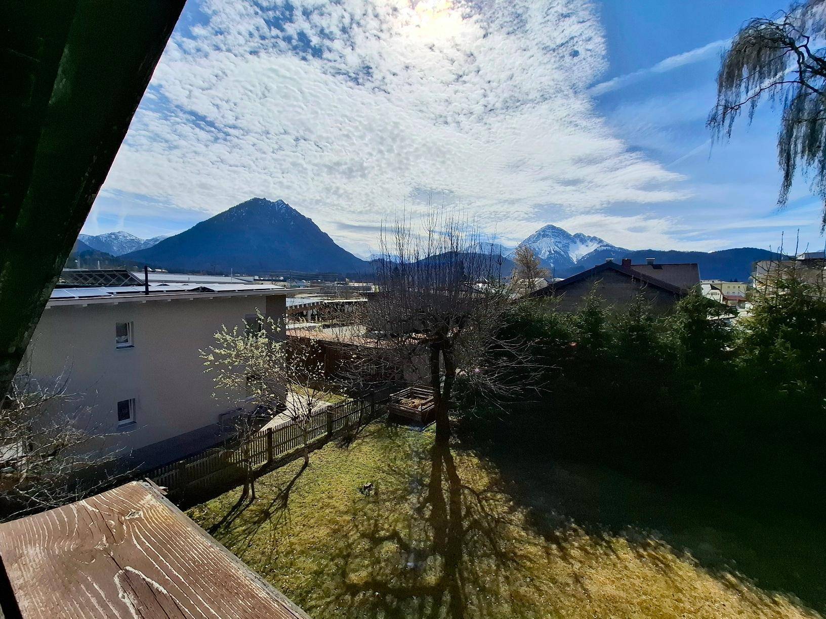 Sonniger Ausblick vom Balkon auf den grünen Garten und die majestätische Berglandschaft.