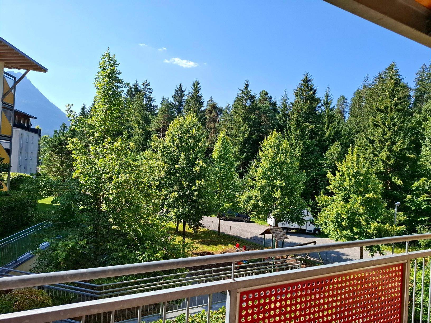 Weitläufiger Blick vom Balkon auf grüne Wälder und die umliegende Berglandschaft unter blauem Himmel.