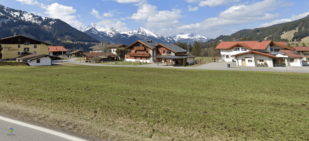 Panoramablick auf ein Bergdorf mit traditionellen Häusern, grünen Wiesen und majestätischen schneebedeckten Gipfeln.