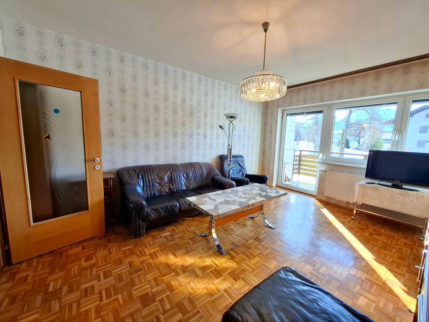 Helles Wohnzimmer mit Ledersofas, Parkettboden und Zugang zu einem Balkon.