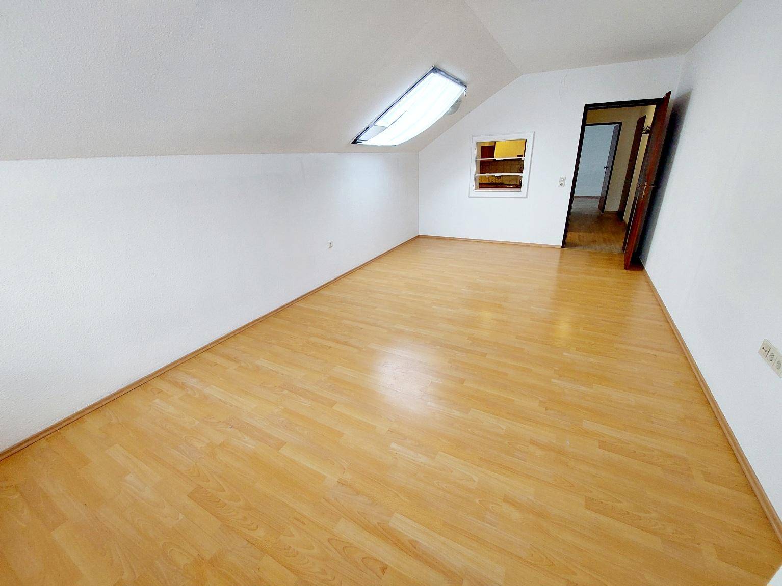 Heller Raum im Dachgeschoss mit schrägen Wänden, Laminatboden und einem Dachfenster.